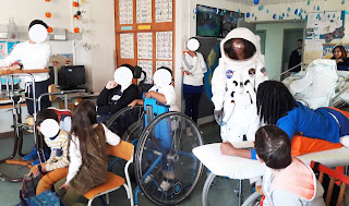 Um grupo de alunos e técnicos olha para a entrada de um astronauta real na sala da escola