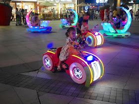 little girl riding an electric toy vehicle at night in Zhongshan, China