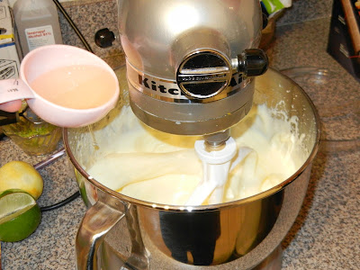 a stand mixer with cake batter in the bowl and lemon being poured into the batter. 