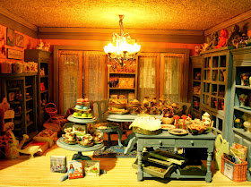 The first floor fo a modern miniature shabby chic shop, with blue cabinets displaying a range of dinnerware and decorative items.