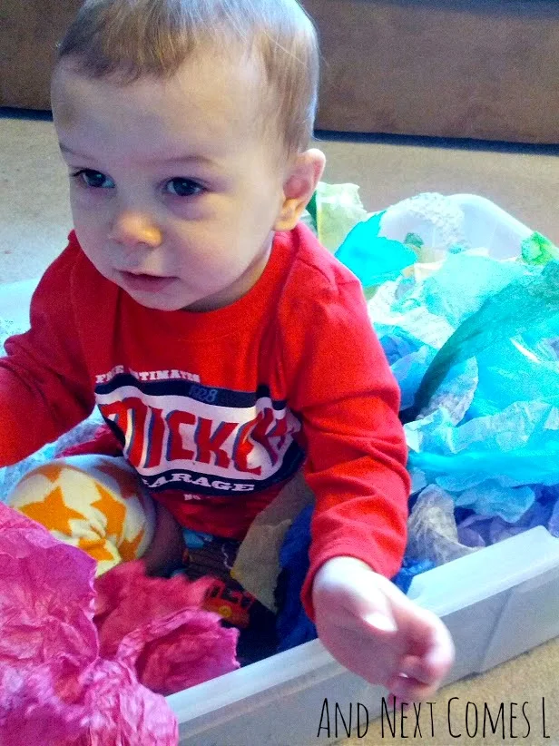 K sitting in tissue paper sensory bin from And Next Comes L