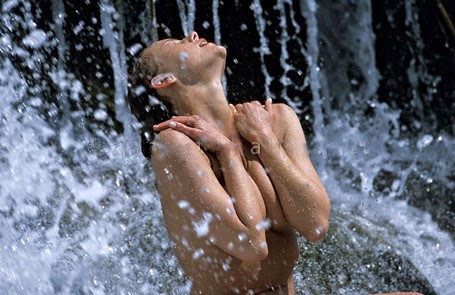 torso de mujer desnuda con manos apoyadas sobre los hombros bañándose en una cascada