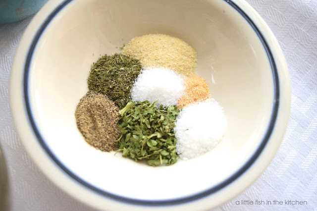 A small ceramic bowl is filled with an array of colorful dried spices. Measures of each, dried dill, parsley, onion powder, garlic powder, salt and ground black pepper are arranged in the bowl. This is the seasoning mix for homemade buttermilk ranch dressing.