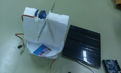 Detalle de primer prototipo de un sistema motor capaz de orientar una placa solar fotovoltaica hacia cualquier foco de luz, construido con corcho blanco, bridas, un CD, dos servomotores y otros materiales reciclados.
