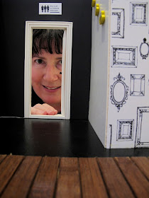 Woman peering through the door to the toilet in a modern dolls' house miniature cafe.