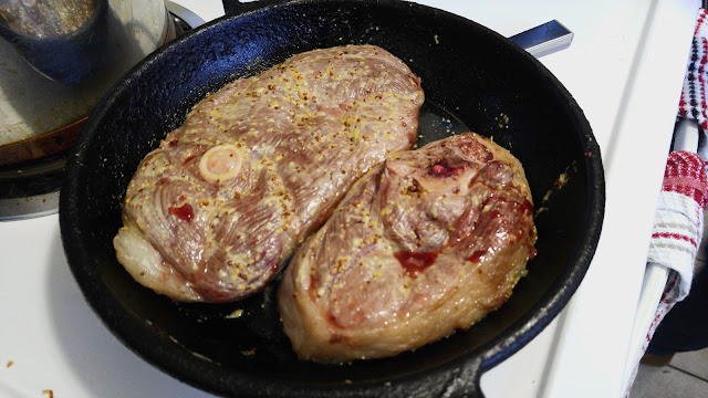 Two lamb leg chops in a cast iron skillet just out of the oven, the lamb meat looks slightly greyish with a bit of blood seeping out on top.