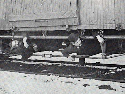 Two hobos ride the rods on the underside of a boxcar. Public domain photo
