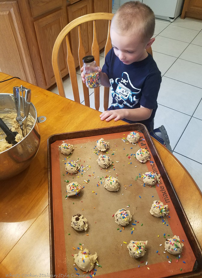 Antonio is helping grandma bake these best ever peanut butter chocolate chip cookies and pouring sprinkles on them