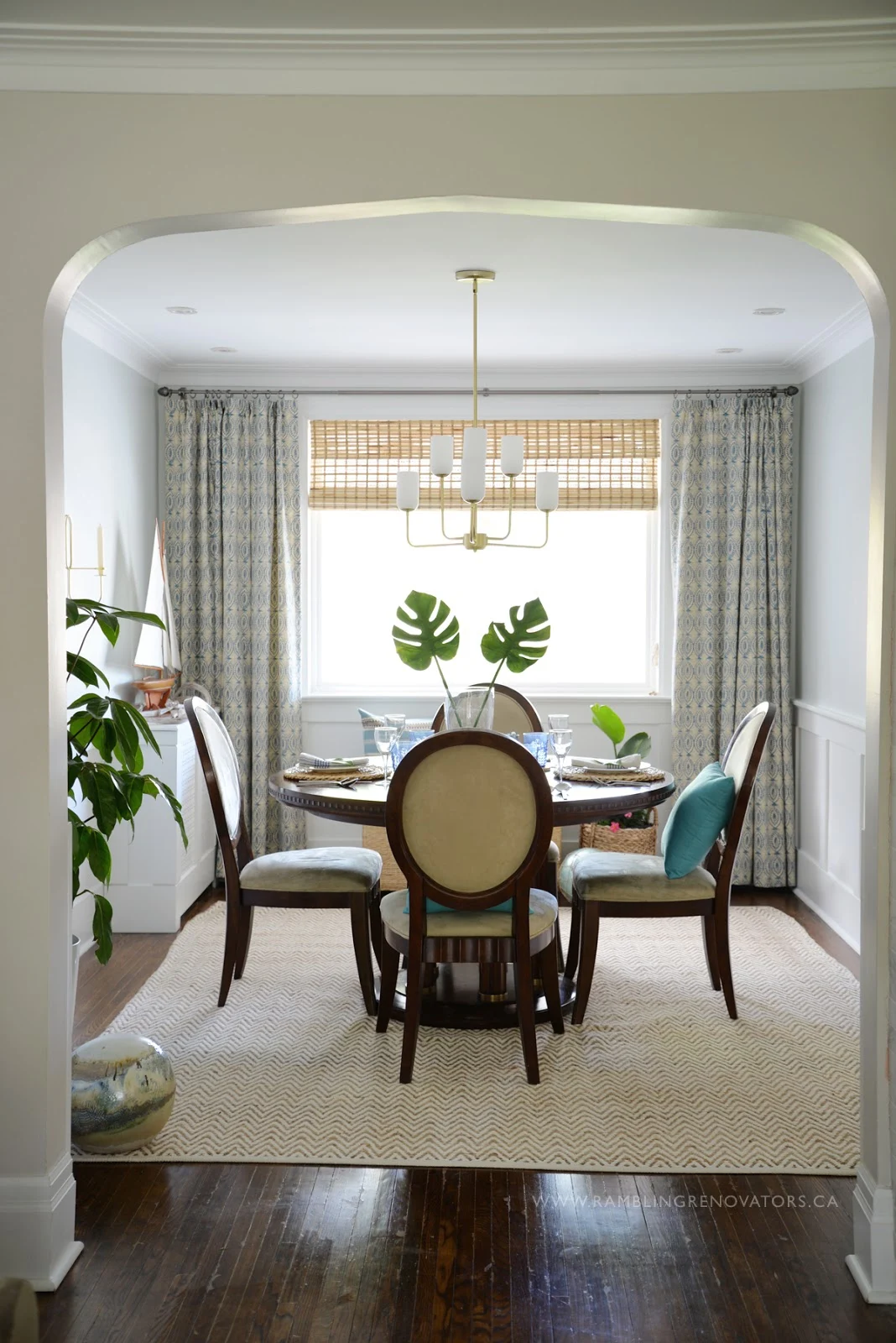 Ramblingrenovators.ca | tropical dining room, round dining table, gold chandelier, bamboo blind, naga blue curtain