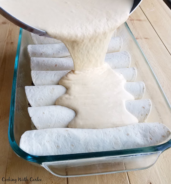 The perfect use for leftover pulled pork! These pulled pork enchiladas are part BBQ and part enchilada. They are creamy, cheesy and oh so good! pouring sour cream cheese sauce over a pan of rolled enchiladas