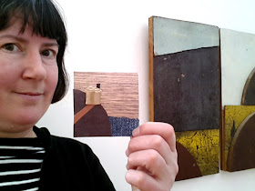 A woman holding up her collage in front of a work by Rosalie Gascoigne in The Daylight Moon exhibition.