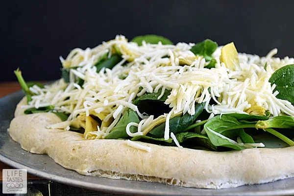 Spinach Artichoke Pizza Recipe | by Life Tastes Good is like eating one of your favorite dip recipes in pizza form! The crust is smothered in an easy-to-make, creamy white Gruyere cheese sauce and then topped with fresh spinach, marinated artichoke hearts, and even more cheese. This pizza smells so good while baking and tastes even better! #SundaySupper