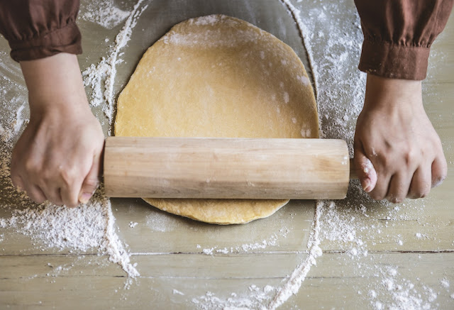 Man using rolling pin to roll out dough with flour on table