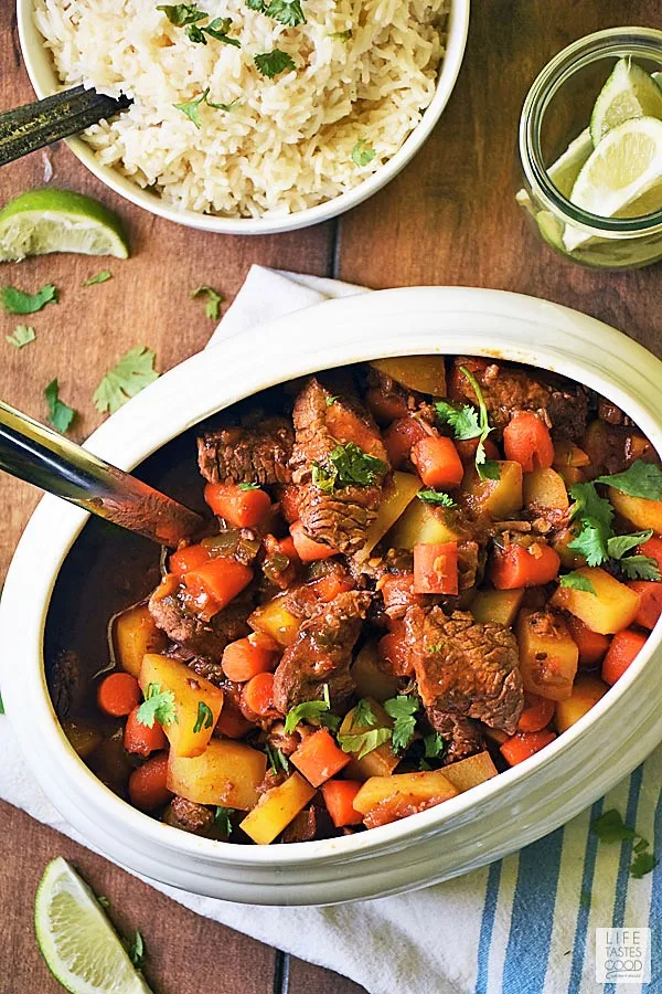 Puerto Rican Beef Stew, Carne Guisada, in a white serving dish with a side or rice and limes