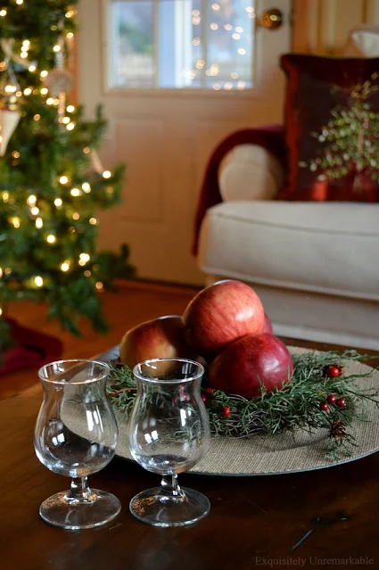 Rustic Christmas with tree lit in background and apples and brandy glasses on table