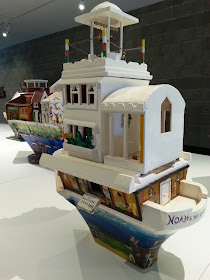Miniature wooden painted artist's arks on display in a gallery.