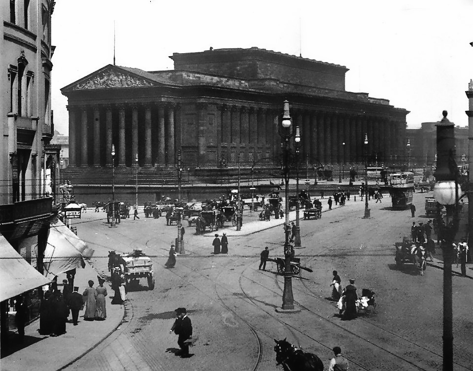 Lime Street, photographed from an elevated position. St George's Hall is prominent.
The streets are cobbled and populated with carts, pedestrians and horses.
The clothing styles suggest the late 19th century.