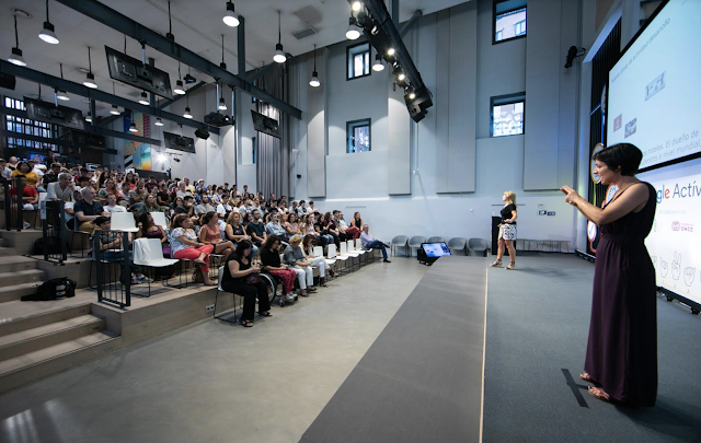 Mujer en un escenario da una conferencia con lenguaje de señas para un auditorio de personas sordas.