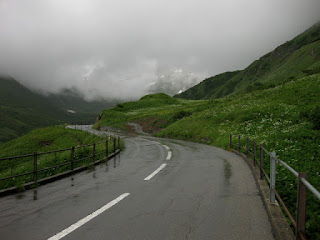 Flowers line the slick roads, approaching a snow-streaked peak on the way to the Oberalppass.