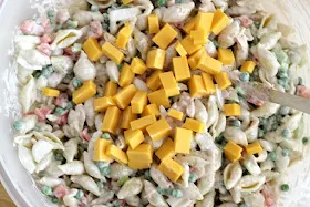 creamy tuna pasta salad in bowl with spoon ready to mix in cheese