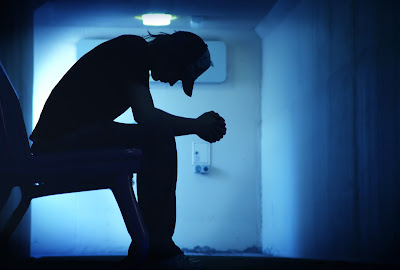 Picture of man silhouette leaning over with elbows on knee. 