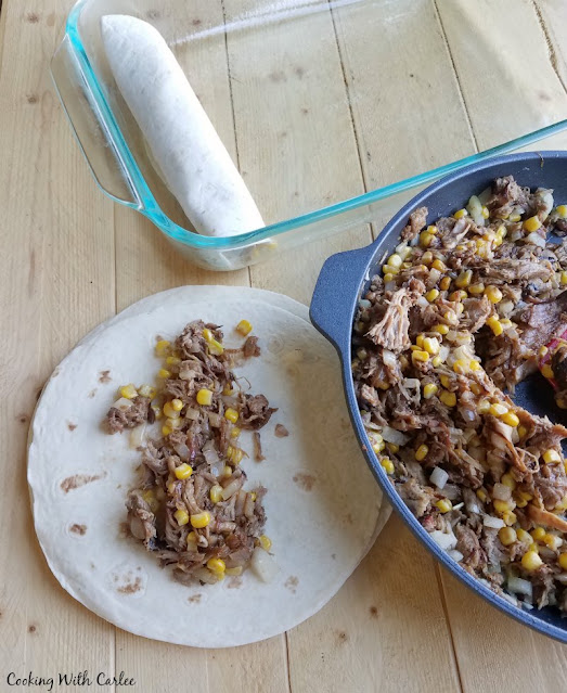 The perfect use for leftover pulled pork! These pulled pork enchiladas are part BBQ and part enchilada. They are creamy, cheesy and oh so good! pan of bbq pulled pork with corn and some on a tortilla being rolled into an enchilada