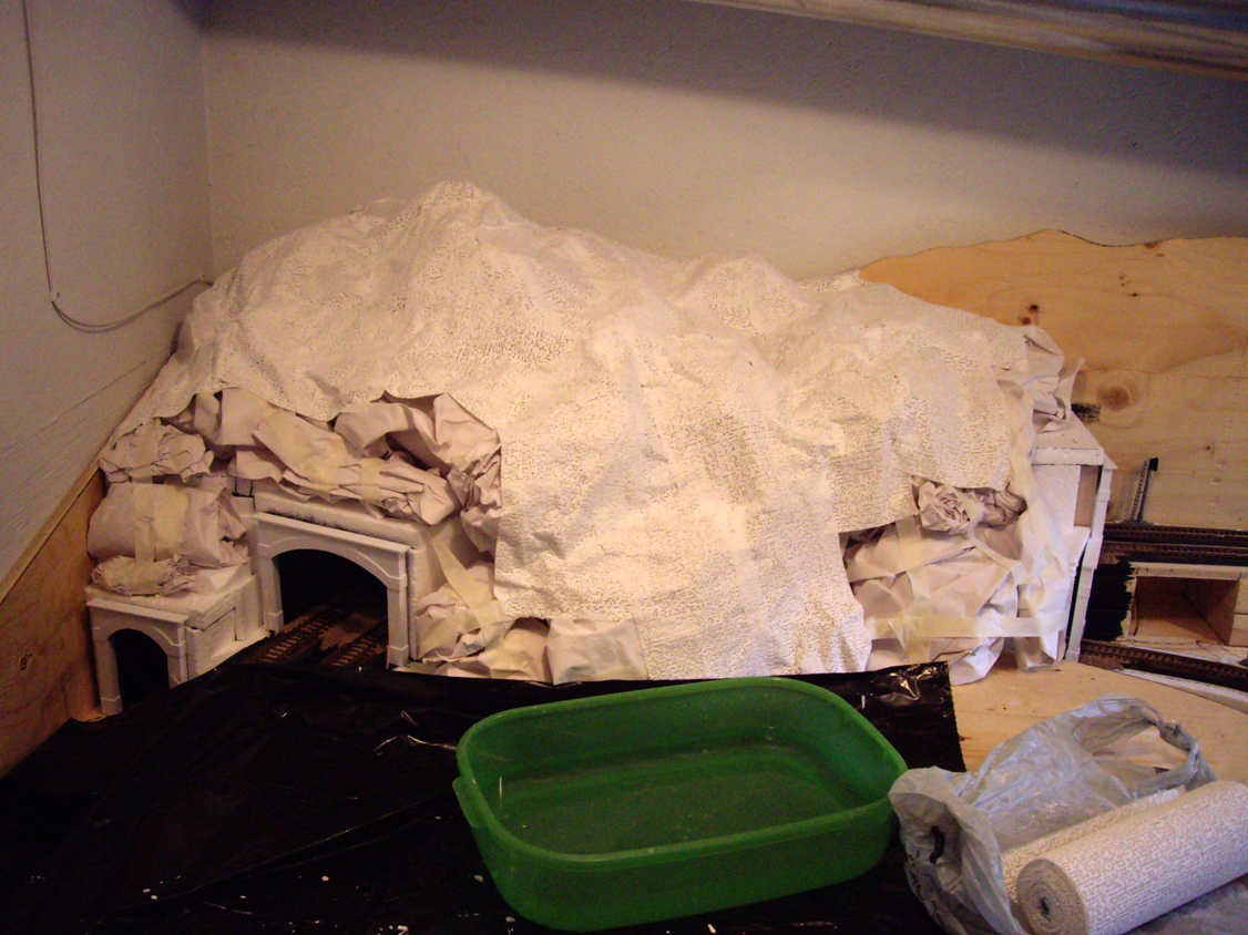Plaster cloth being applied to crumpled paper balls on foam tunnel structure to form a mountain