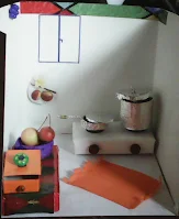 diorama bucatarie: aragaz, oala si tigaie din carton acoperit cu staniol argintiu, bufet, sertar portocaliu si diverse decoratiuni in miniatura