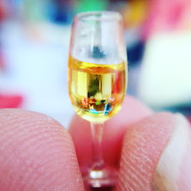 Macro photograph of a one-twelfth scale glass of wine held by several fingers.