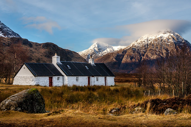 Photo of Blackrock Cottage in the sun with snow capped Buachaille Etive Mor