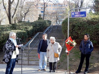 A un lado Montserrat Galcerán lee, al fondo, junto a la placa, algunos miembros de la familia.