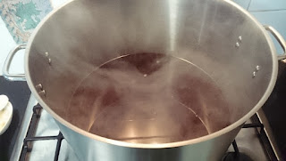 A large pot of beer simmering over a gas hobb with steam rising toward the camera.
