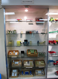 Glass display case containing shelves with various sets and pieces of metal dolls' house furniture displayed on them.