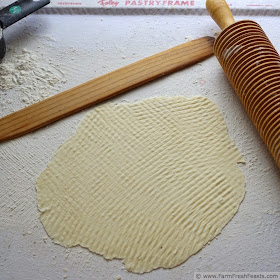 a floured pastry cloth with a piece of rolled lefse, a rolling pin, and the stick to carry the lefse to the griddle