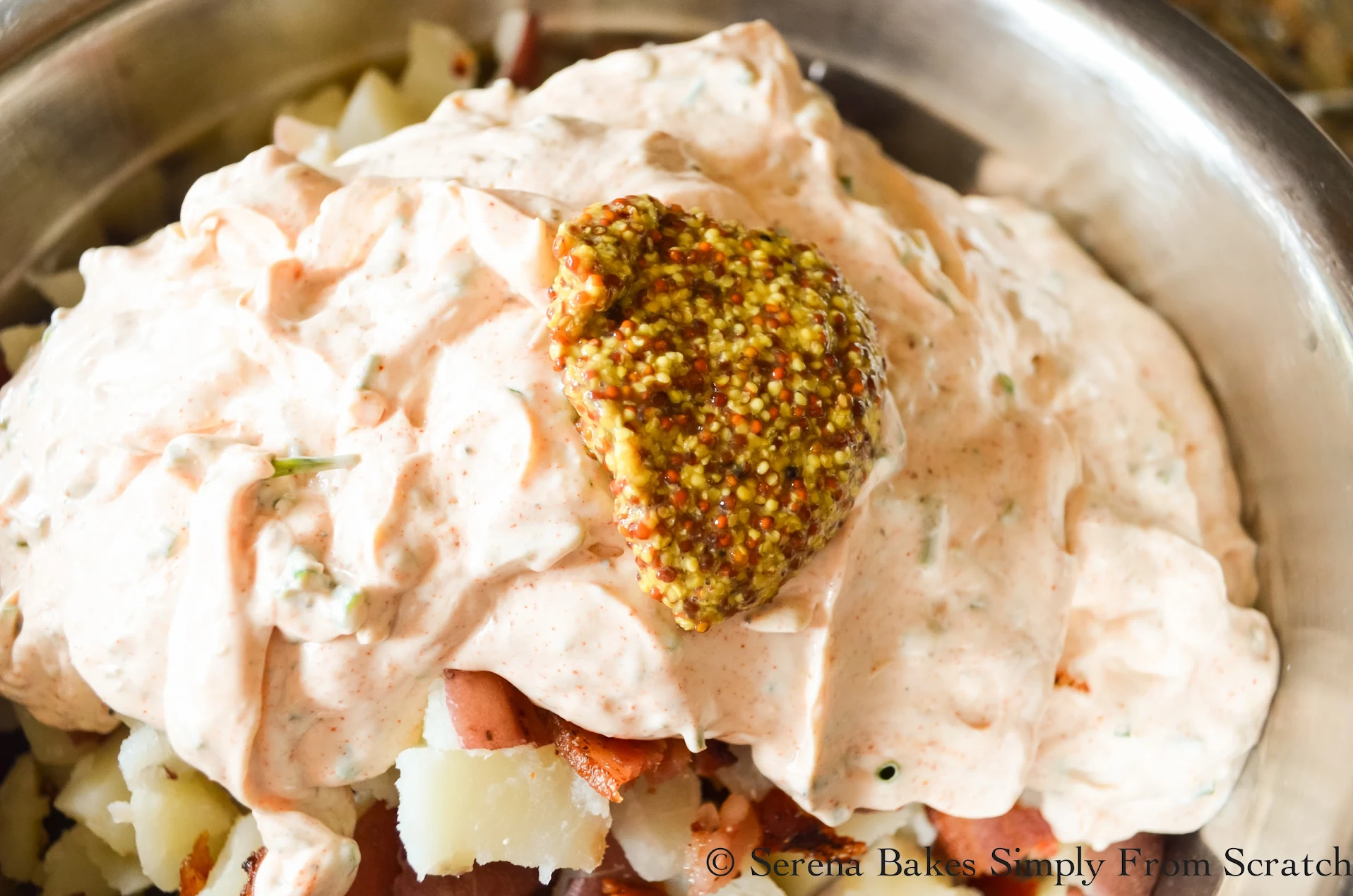 Sour Cream mixture poured over the top of diced red potatoes and bacon in a stainless steel bowl.
