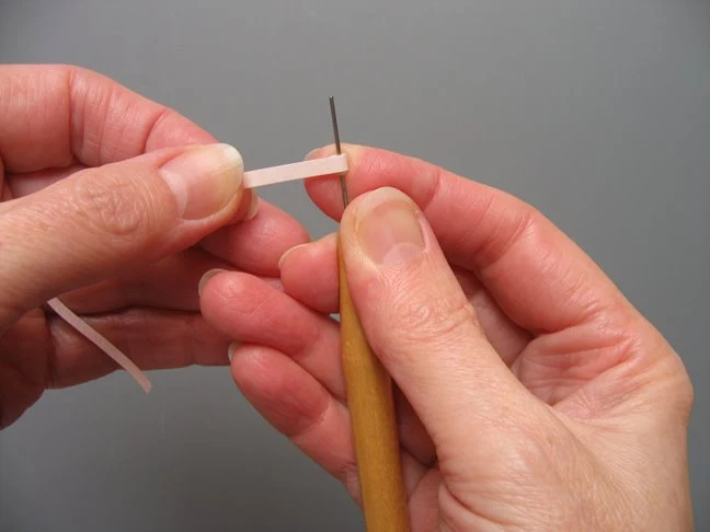 hands holding a rolled paper strip on a needle tool
