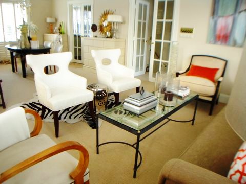 Living room in Ron van Empel of Empel Collections' home with zebra print rug, silver Chinese garden stool, white armchairs and a taupe sofa with orange and white graphic print accent pillows