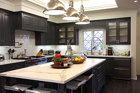 Kitchen after remodeling with Calcutta Gold marble countertops, dark brown painted wood cabinets, new windows, subway tile backsplash and pendant kitchen island lighting