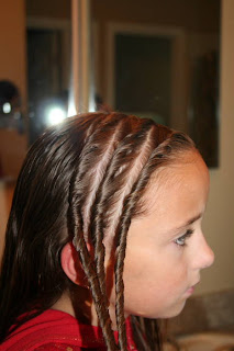 Side view of Young girl's hair being styled into "Triple Twists and Messy Buns"