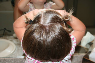 Back view of young girl's hair being styled into "Two Messy Twists on Top" Hairstyle