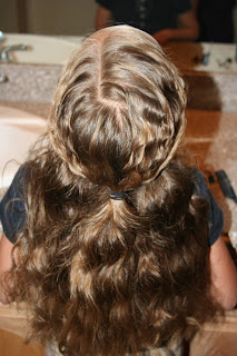 Back view of young girl's hair being styled into "Curls After Triple Twists w/ Messy Buns" hairstyle