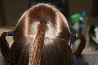 Back view of young girl's hair being styled into "Holiday Twisty Buns" hairstyle