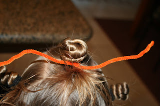 Close up view of young girl's hair being styled into "Holiday Twisty Buns" hairstyle with an orange pipe cleaner