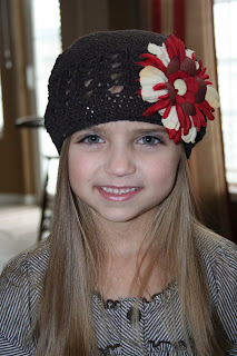 Portrait view of young girl modeling chocolate-brown beanie with a red and cream big flower