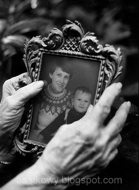 Ilustracja prezentująca dłonie staruszki trzymające starą fotografię w zdobionej ramce.
