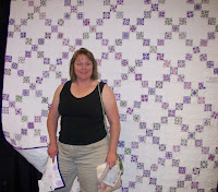 Pam in front of a purple and white nine patch quilt that she made for her sister