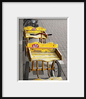 Framed photo of a child's bright yellow antique wagon on drab sidewalk