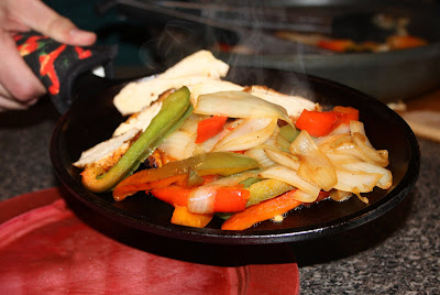 hand holding skillet with chicken, bell peppers, and onions