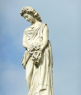 La doncella Estatua de mujer de pié con ramo de flores sobre su regazo.