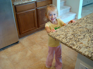 Young girl in pink and yellow in kitchen holding onto countertop